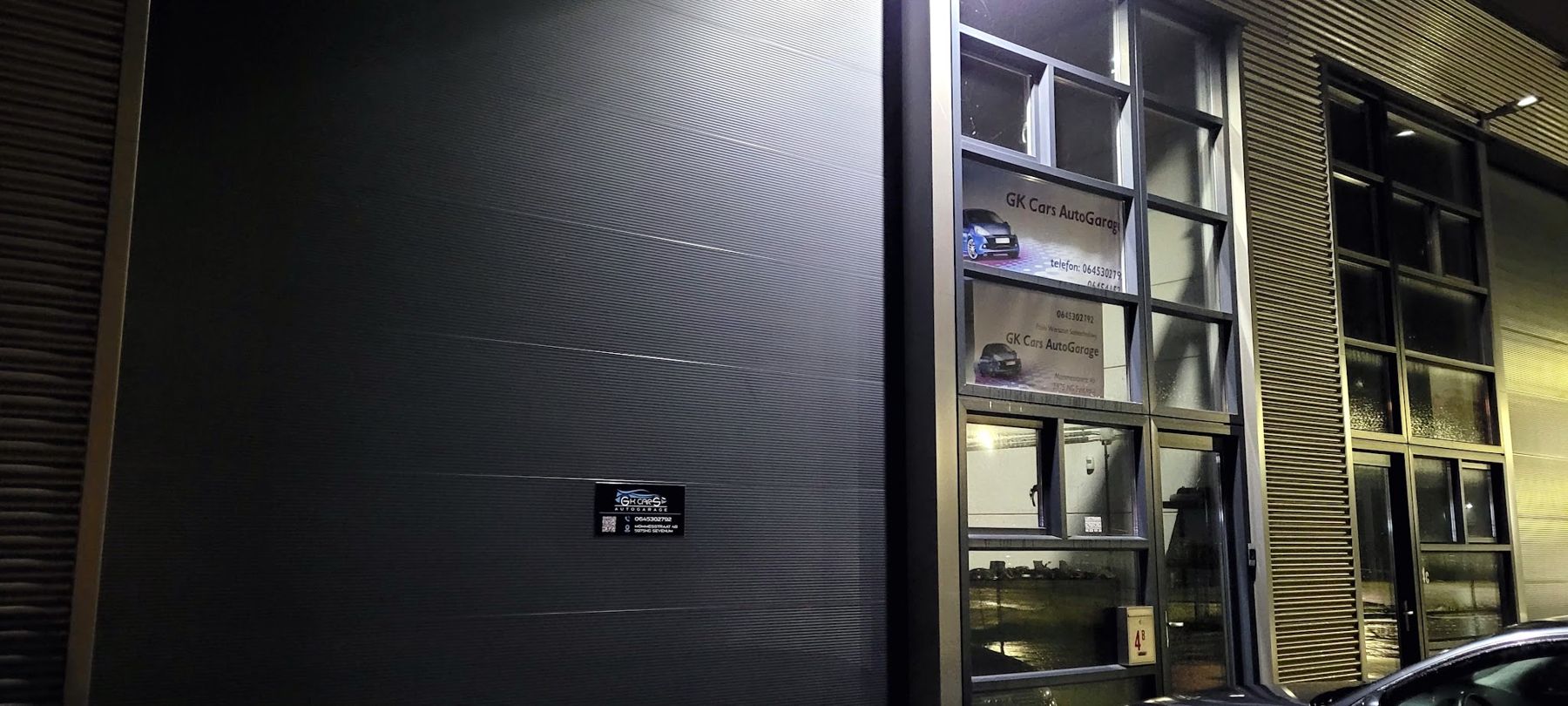 De bedrijfsunit van GK Cars AutoGarage in de avond, met de naam op het raam